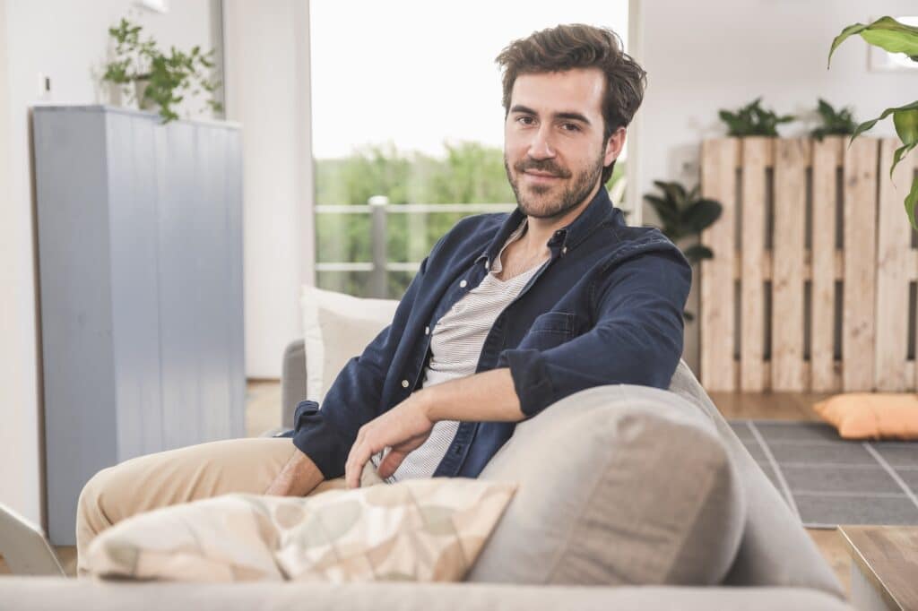 Young man sitting on couch at home, smiling